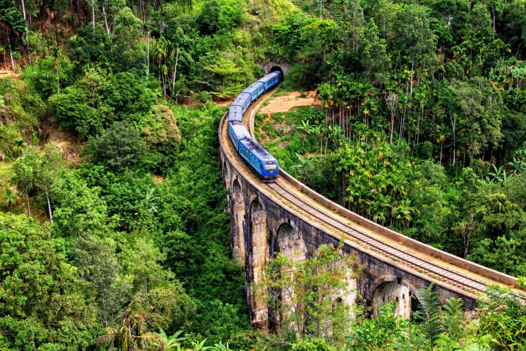 A blue train traverses the iconic Nine Arch Bridge in Ella, surrounded by lush Sri Lankan forests.